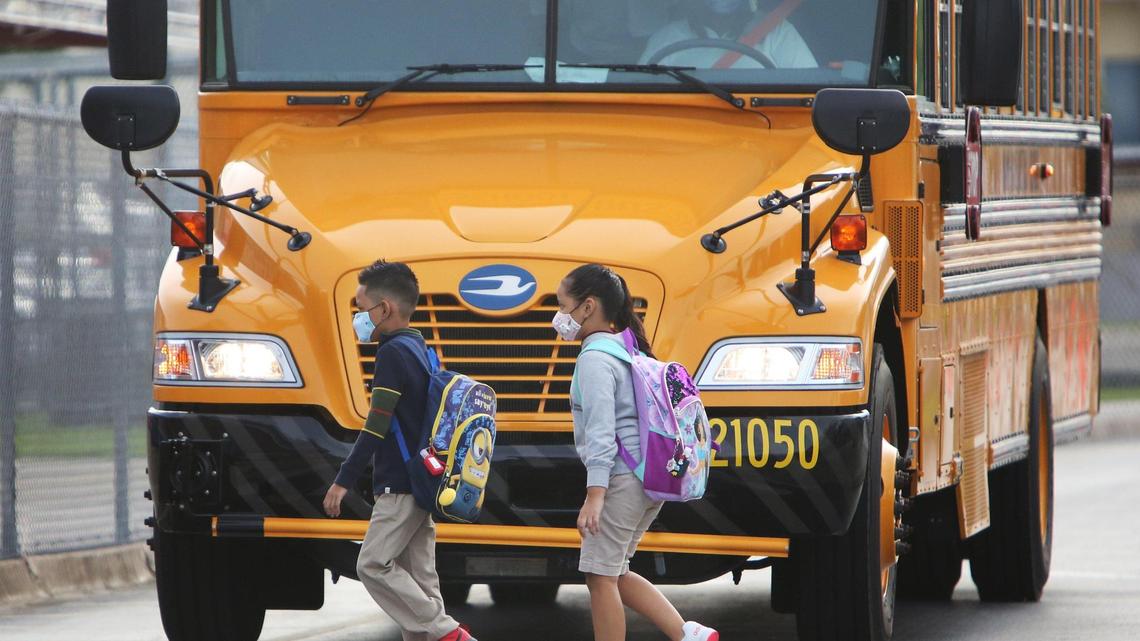 Students wearing masks cross in front of a school bus at Carrie P. Meek/Westview K-8 on Monday, the first day back of in-person learning for pre-k, kindergarten and first-graders in Miami-Dade public schools.