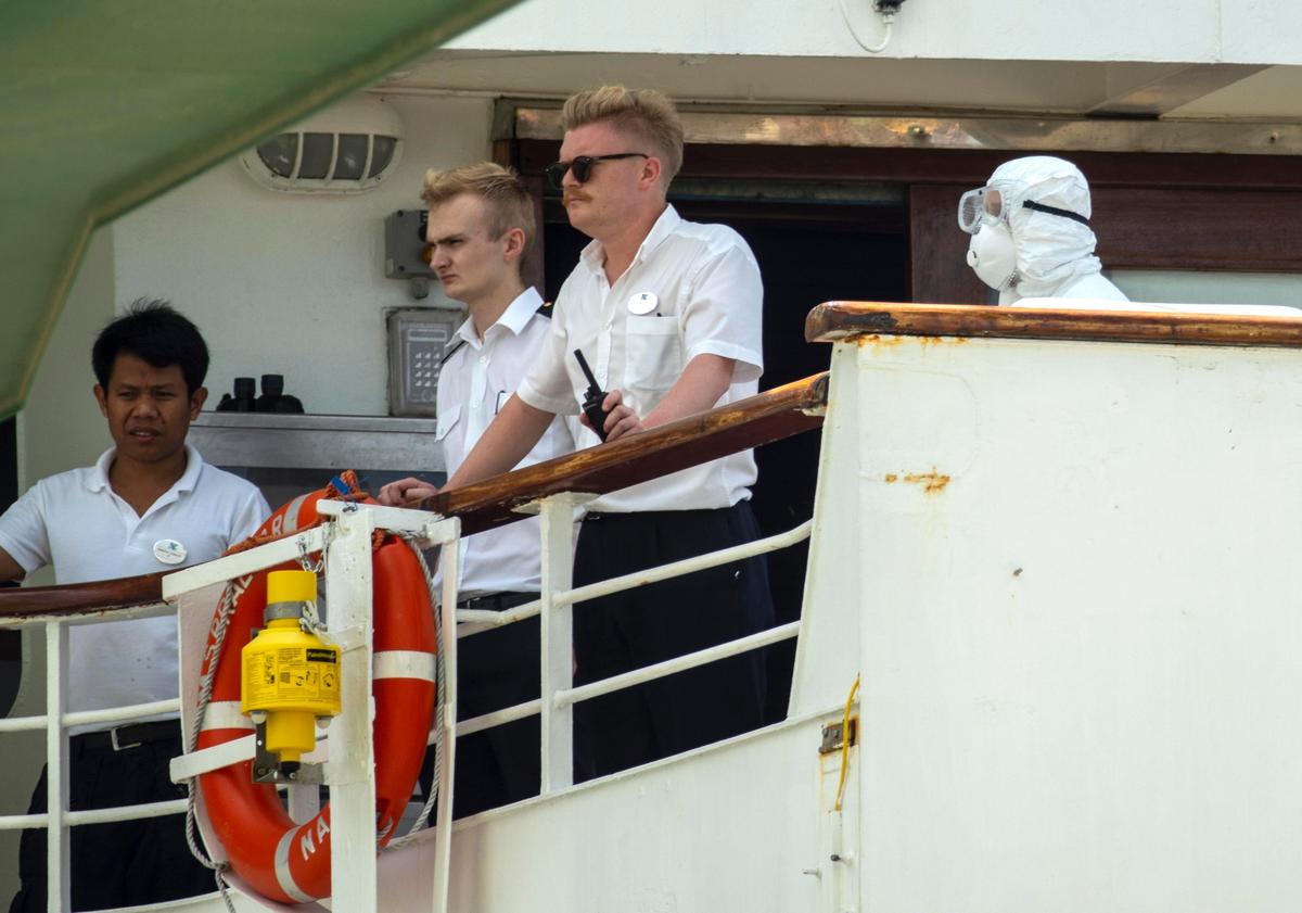 Crew members of the Braemar cruise ship and a person dressed in protective clothing look out at the port while docked in Mariel, Cuba, on Wednesday, March 18, 2020. The ship docked in Cuba after being turned away from several ports because of five cases of COVID-19 on board.