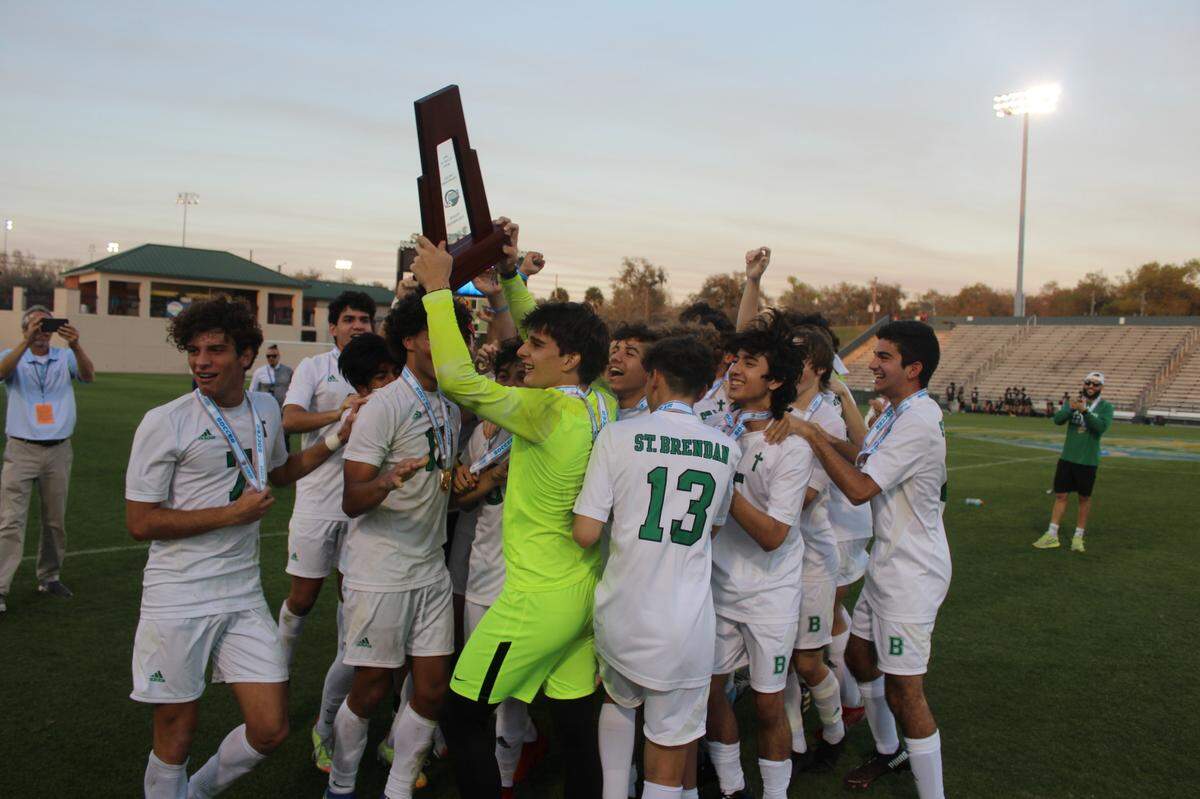 St. Brendan’s soccer players celebrate with their state championship trophy moments after they defeated Orlando Bishop Moore 1-0 in the Class 4A final on Thursday at Spec Martin Stadium in DeLand.
