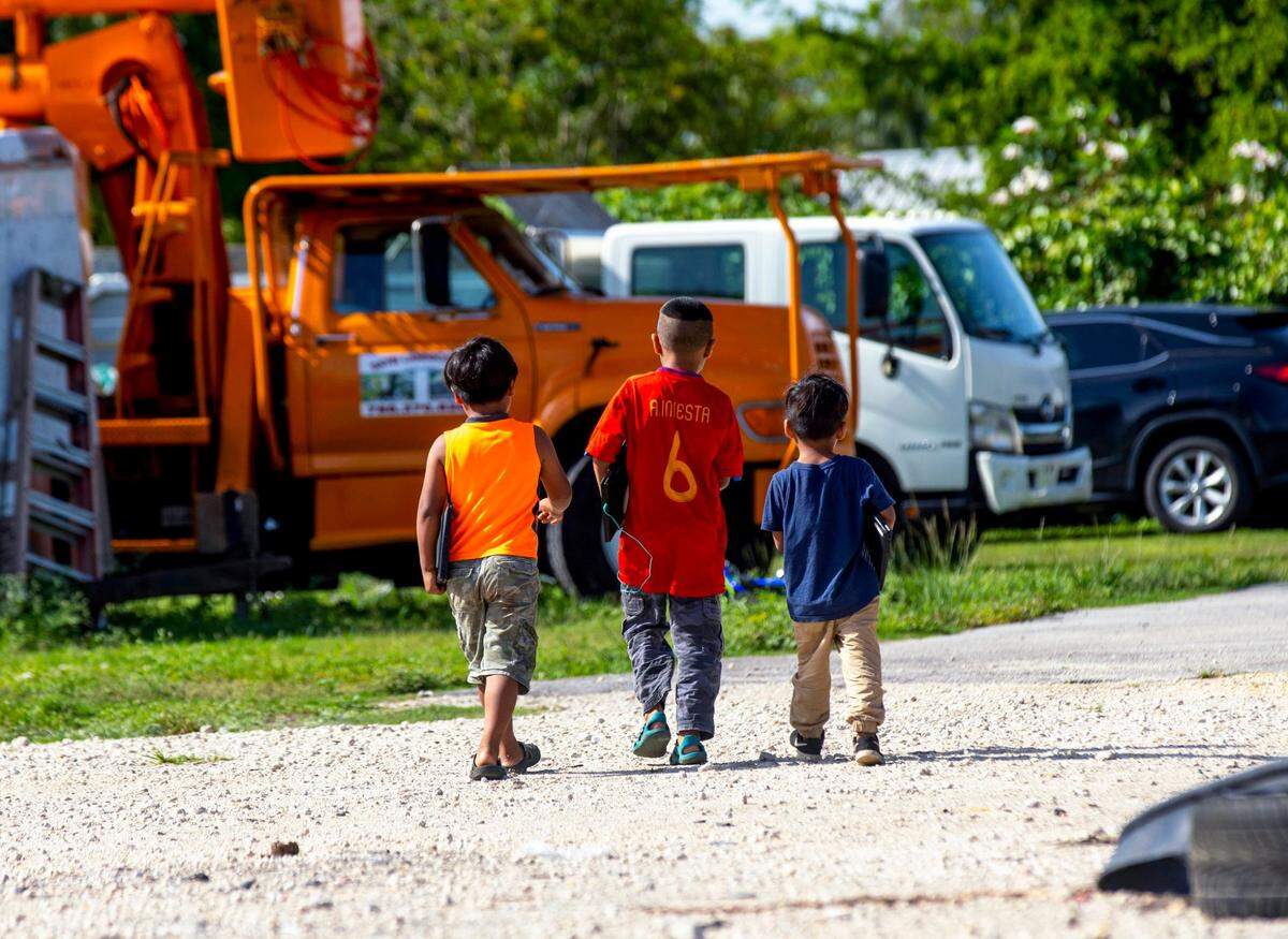 Three migrant boys walk to the area in the camp designated for virtual learning with their Miami-Dade County School-provided laptops in tow during the coronavirus pandemic in South Florida on Thursday, May 21, 2020.