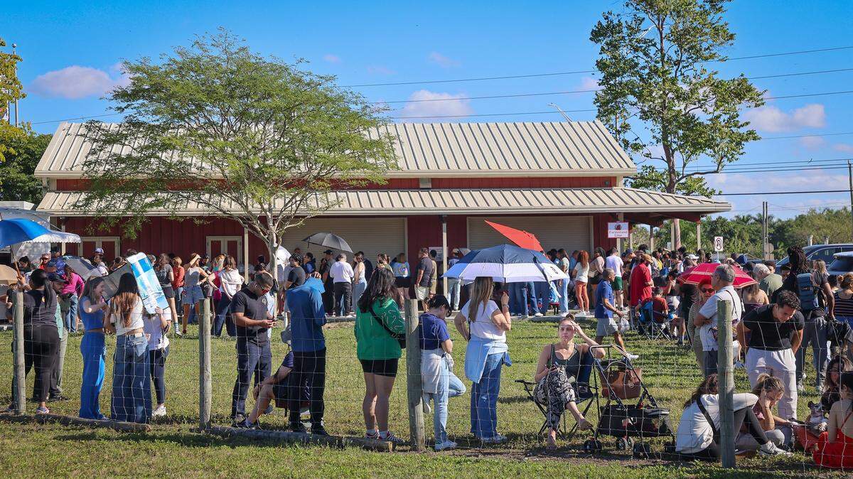 Customers line up under umbrellas, in chairs, and seated on the grass for more than two hours to place their cinnamon rolls orders. Knaus Berry Farm opened at its new location, offering shakes, baked goods, and the cinnamon rolls for which it became famous. At the same time, some customers wanted shakes, most lined up for cinnamon rolls, and some even arrived the night before to ensure success on Monday, December 22, 2025, in Redlands, near Homestead, Florida.