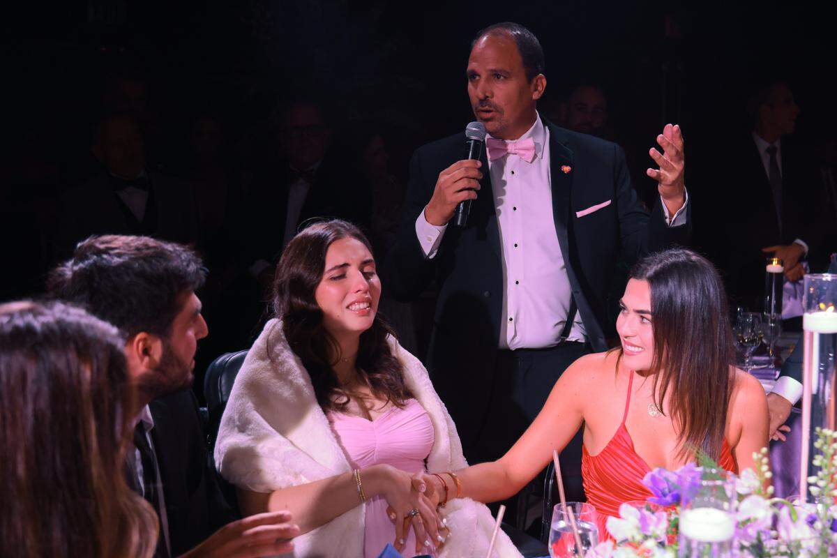 Amanda Puig, right, holds the hand of her sister, boating accident survivor, Katerina “Katy” Puig, as their father, Rudy Puig Sr., speaks during the Nicklaus Children's Foundation Diamond Ball at the JW Marriott Marquis in Downtown Miami, Saturday, October 18, 2025.