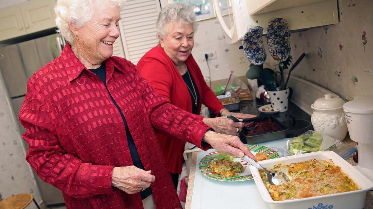 Sandra Reed, left, and Barbara Sims host the annual Three Sisters Luncheon, a holiday meal for those residents of East Ridge Retirement community that don't have relatives nearby. In photo, Sandra serves up a dish called Bonnie's Chicken Casserole