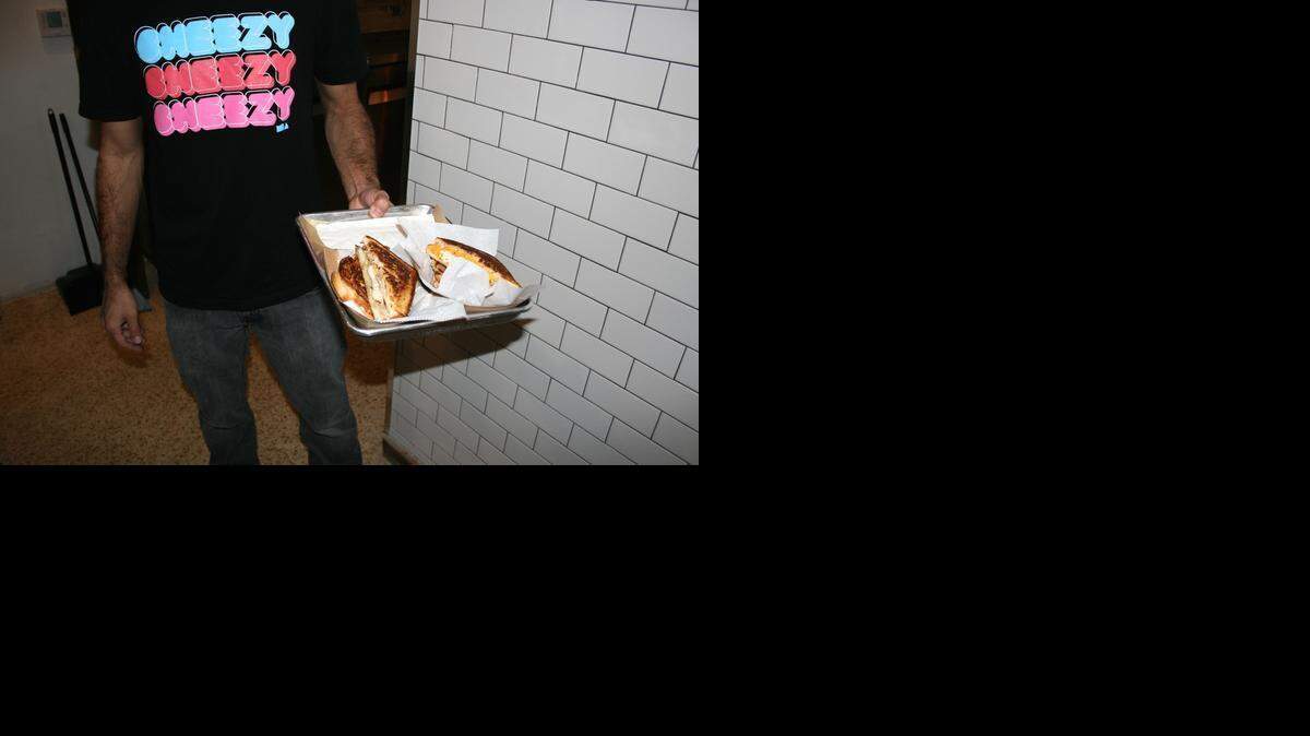 
 A Ms. Cheezious employee holds two grilled cheese sandwiches at the new bricks and mortar, which opened in early February. 
