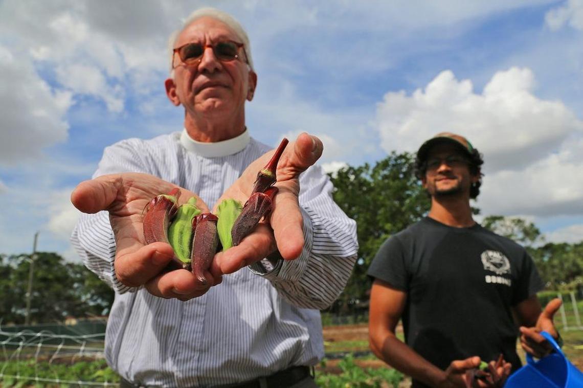 Father Carlos Sandoval holds produce from the farming by Moses Kashem, right, of the land at St. Simon’s Episcopal Church.