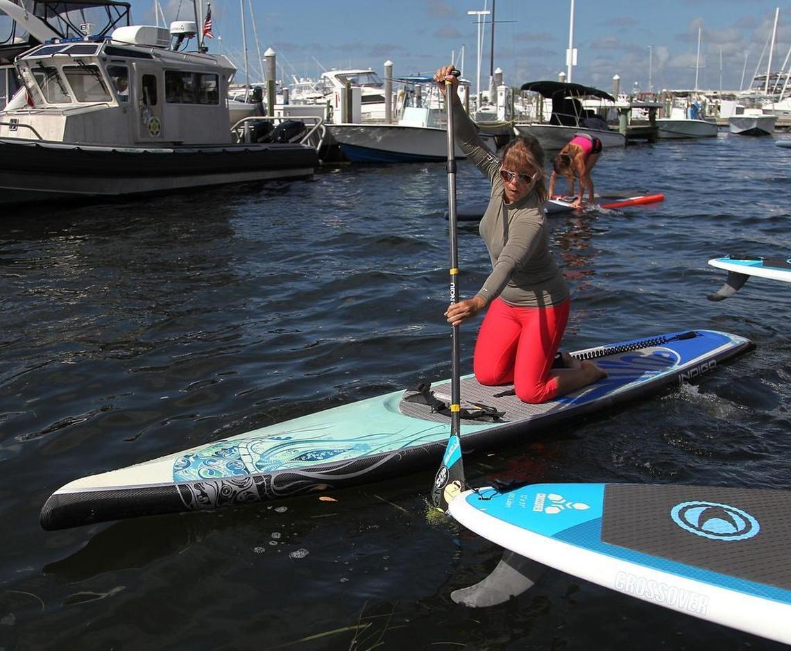 Barbara Perez kneels and paddles toward Biscayne Bay while Violet Llerena, right, gets to feet on her paddleboard during a session of SUP The Workout at the U.S. Sailing Center in Coconut Grove.
