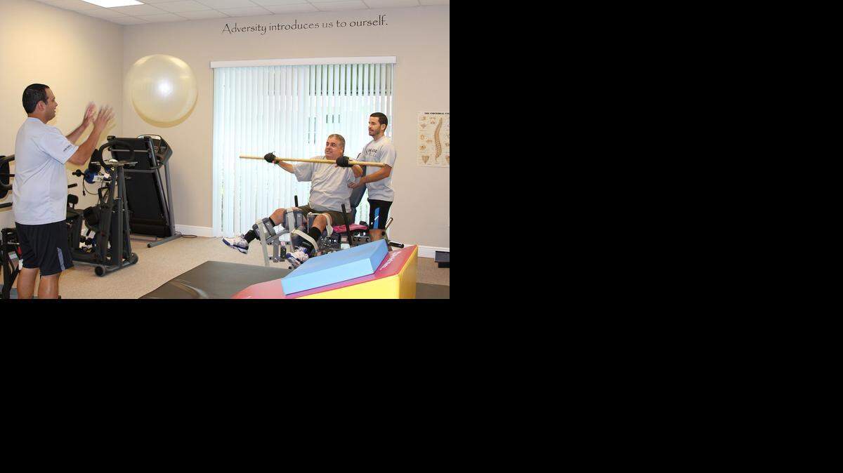 
IN TRAINING: Julio Gutierrez hits a ball to trainer Sachi Gundrania as trainer Osvaldo Reyes supports his back during a hand-eye coordination exercise at "i Am Able Fitness." Gutierrez developed Guillain-Barre Syndrome, which affects his nervous system, after getting a flu vaccine in 2012.
