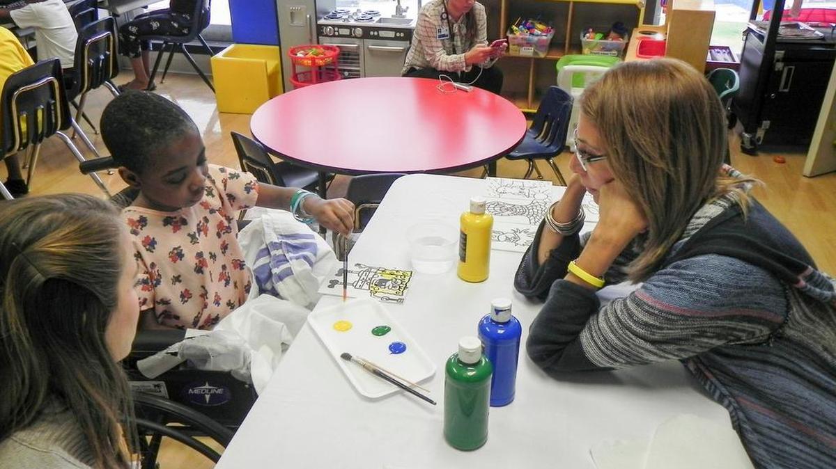 Frida Exantus paints one of the drawings provided by ArtCares for Kids with help from Liz Portuondo (right) and hospital volunteer Barbara Nunez.