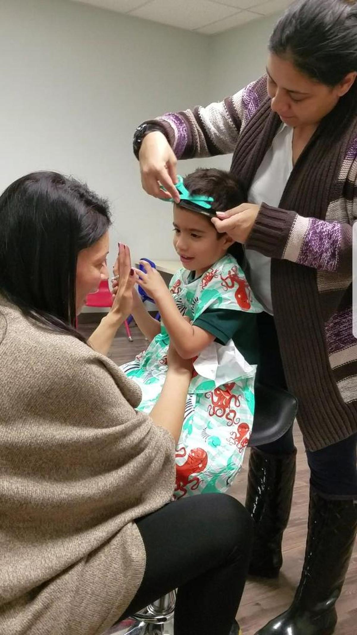 Aidan Lugo, now 4, center, gets his free haircut at a Snips for Autism session at Gomez Behavior Services in Kendall. In front of him is behavioral therapist Priscilla Deal Rossi, behind him is behavioral therapist Giancarla David.