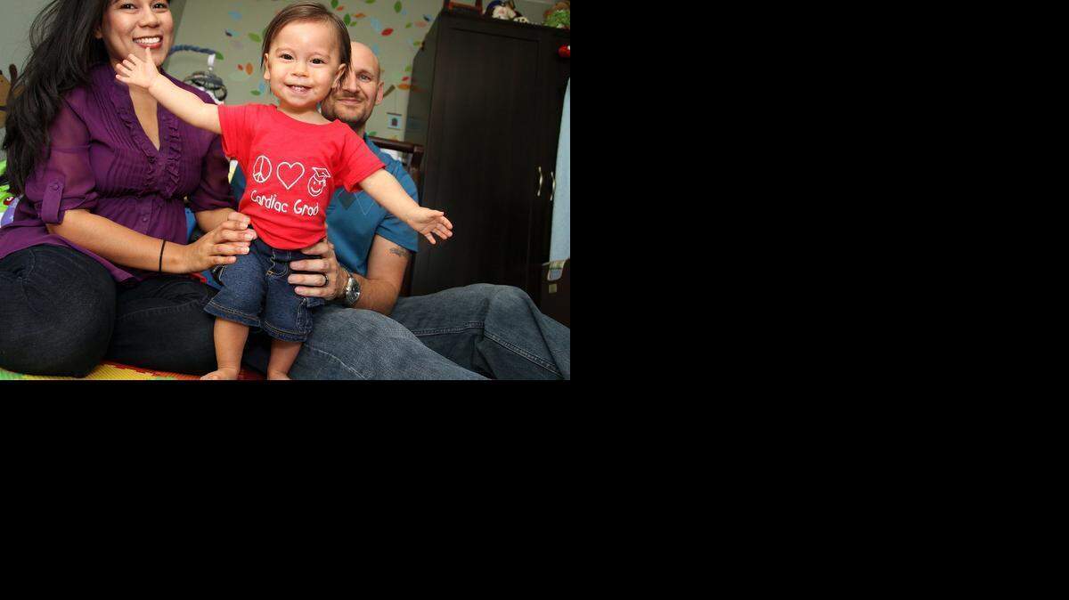 
‘HE’S DOING GREAT’: Elias Graham, 1, with his parents, Betty and Adam Graham, at their West Kendall home.  Elias was diagnosed with heart defects in utero and has undergone two surgeries since birth. 
