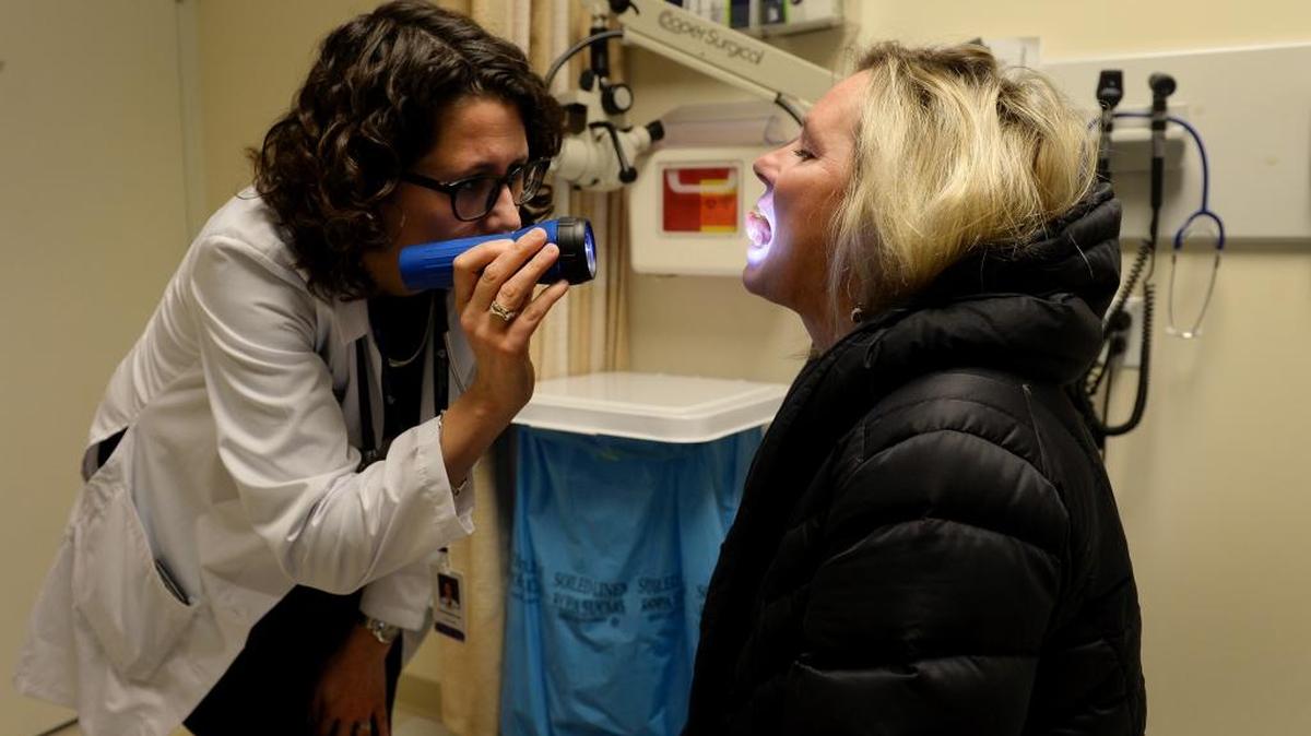 Zofia ‘Zosia’ Piotrowska, left, checks sores in Diane Legg's mouth last month in Danvers, Massachusetts. Legg is undergoing treatment for lung cancer.