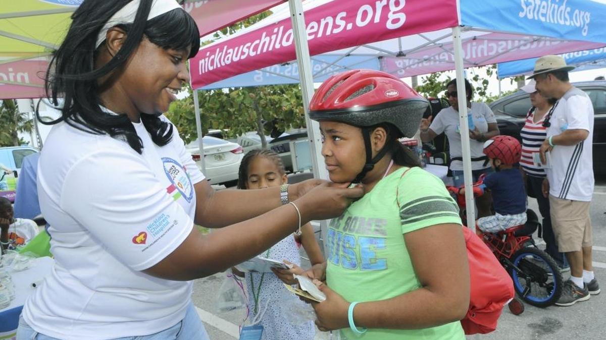 Nicklaus Children's Hospital injury prevention specialist Tara Hills, left, adjusts the chin strap on a new bike helmet for Virginia Walters, 10, of Miramar, during the eighth annual Summer Safety Splash on Saturday, May 14, 2016 at Haulover Beach Park.