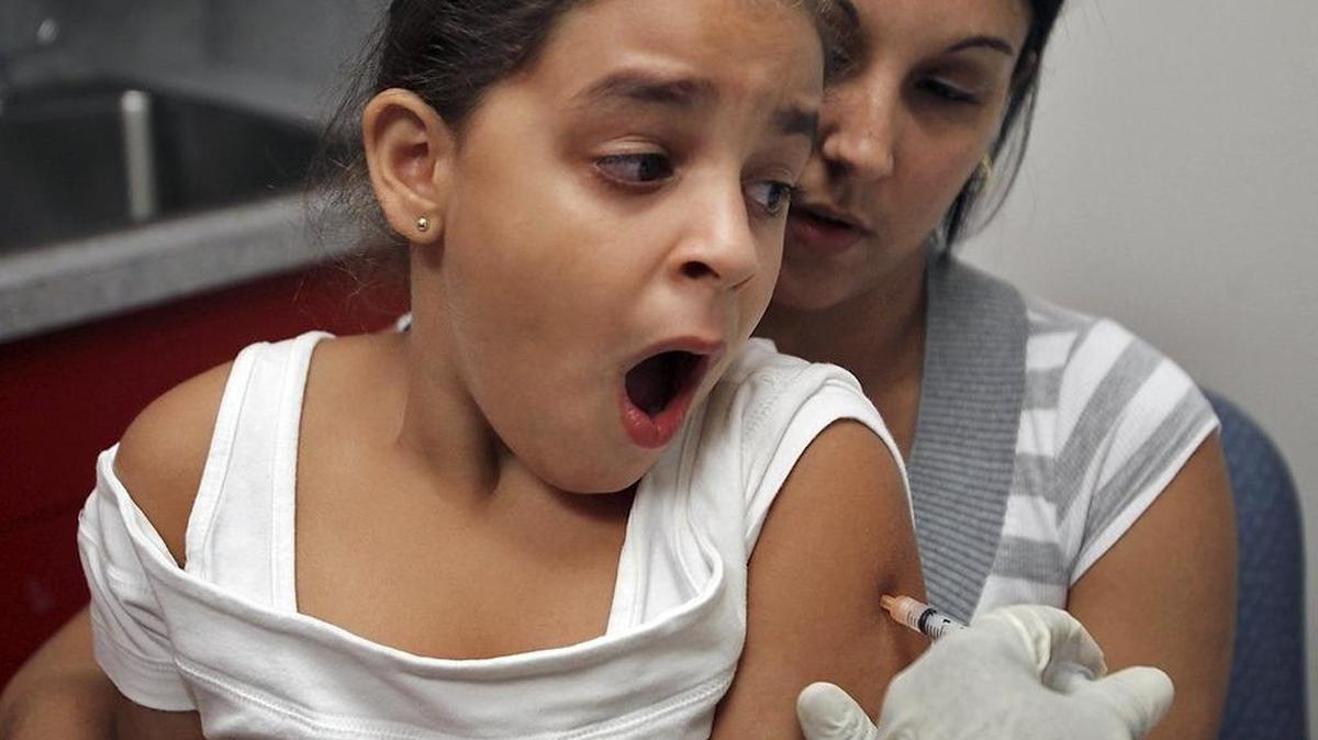 Olivia Magistre Victore, de 7 años y sentada en las piernas de su madre, recibe su vacuna como parte del programa de atención a los estudiantes, en el verano de 2011.