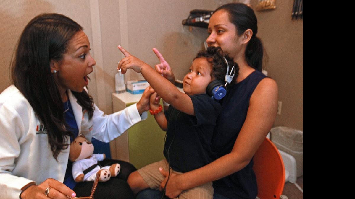 TESTING PRECIOUS HEARING:  Dr. Annie Rodriguez conducts a hearing examination on Henry Figueroa, 3, as his mother, Jylinette Fontani, holds him in one of the pediatric audio booths at UM’s med school recently.