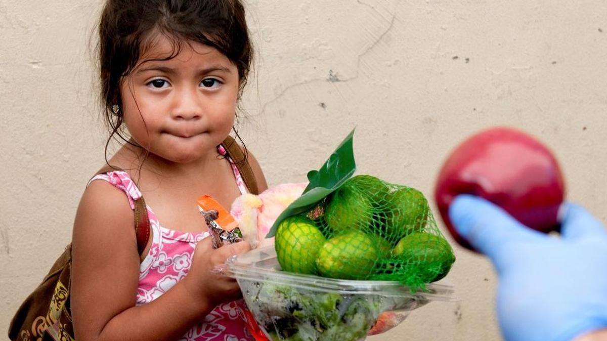 Kasie Pena, 4, looks at one of the volunteers as he offers her an apple at the Glory Temple Ministries in Miami.