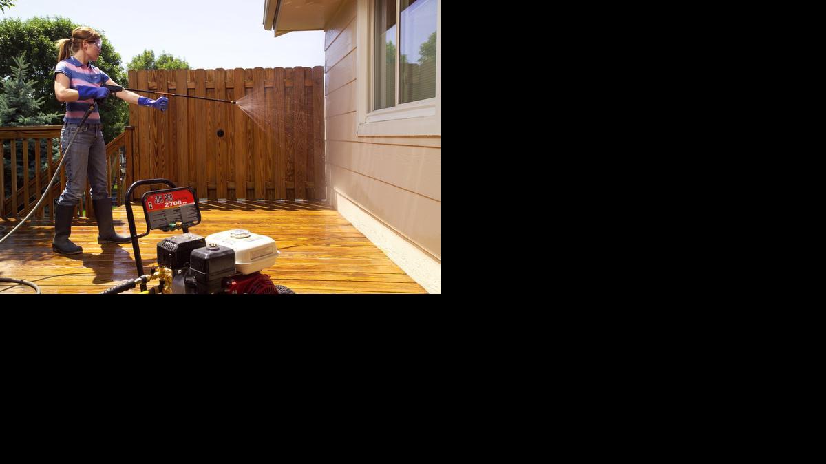 
A woman cleans off overspray by rinsing the siding and windows with clean water at a low pressure to remove chemical residue.
