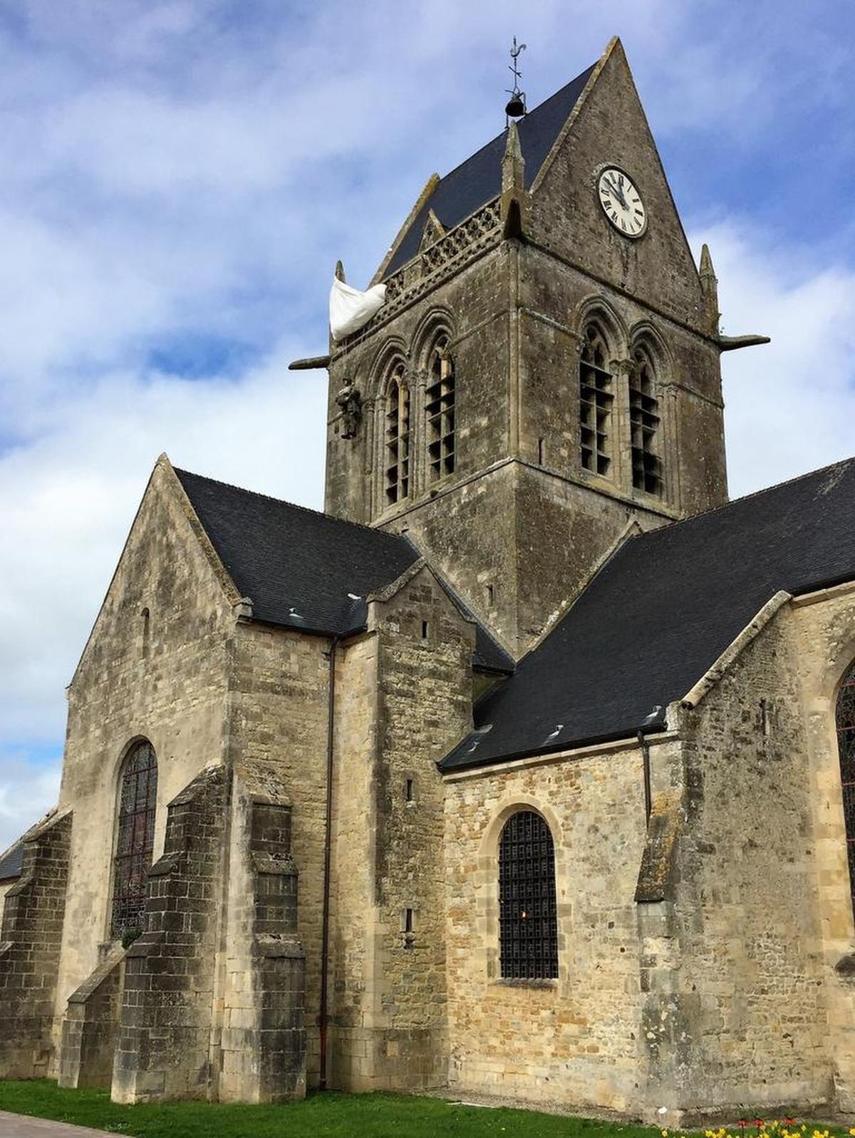 The church of Sainte-Mere-Eglise where mixed units of the U.S. 82nd Airborne and U.S. 101st Airborne Divisions arrived on June 6, 1944. Note the dummy paratrooper that represents John Steele (upper left). Steele, a U.S. paratrooper, hung there limply for two hours, pretending to be dead, before Germans took him prisoner. Steele later escaped.