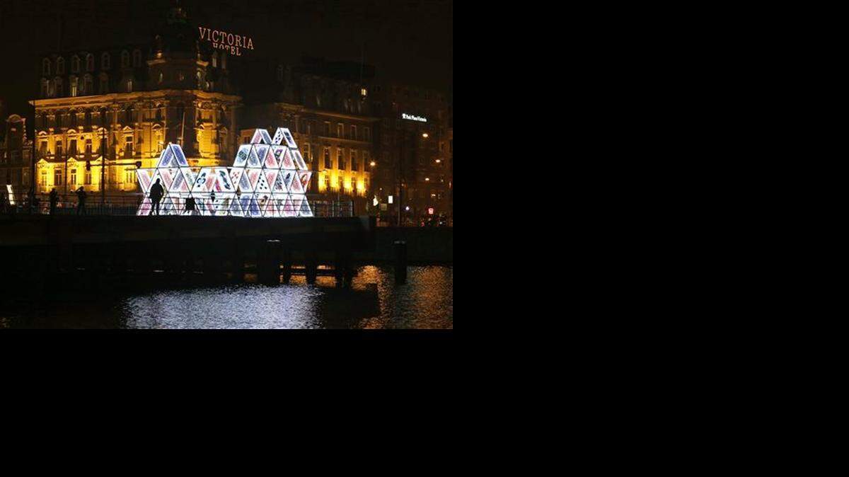 In this Saturday, Nov. 29, 2014 photo, people look at a light sculpture called, "House of Cards," by OGE Creative Group, from Israel, near Central Station in Amsterdam. The sculpture is a playful part of the Amsterdam Light Festival which opened Nov. 27, 2014, with the aim of bringing a little illumination and color into the gloomy days and nights of winter that are settling over the Dutch capital. (AP Photo/Peter Dejong)