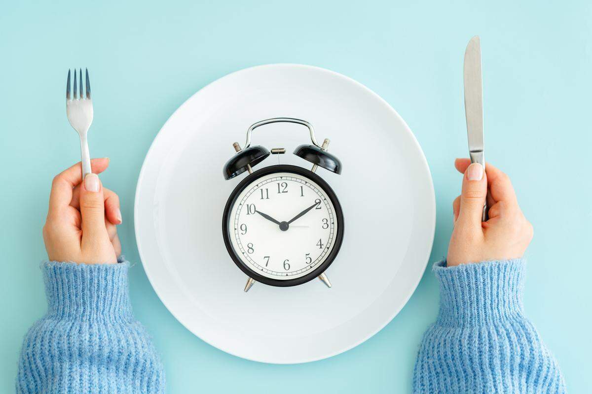 Two hands holding utensils above a plate with an image of a clock on it. 