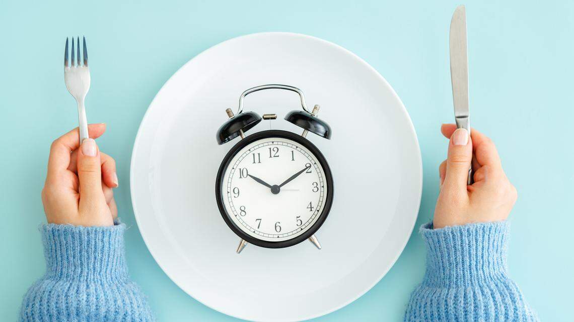 Two hands holding utensils above a plate with an image of a clock on it. 