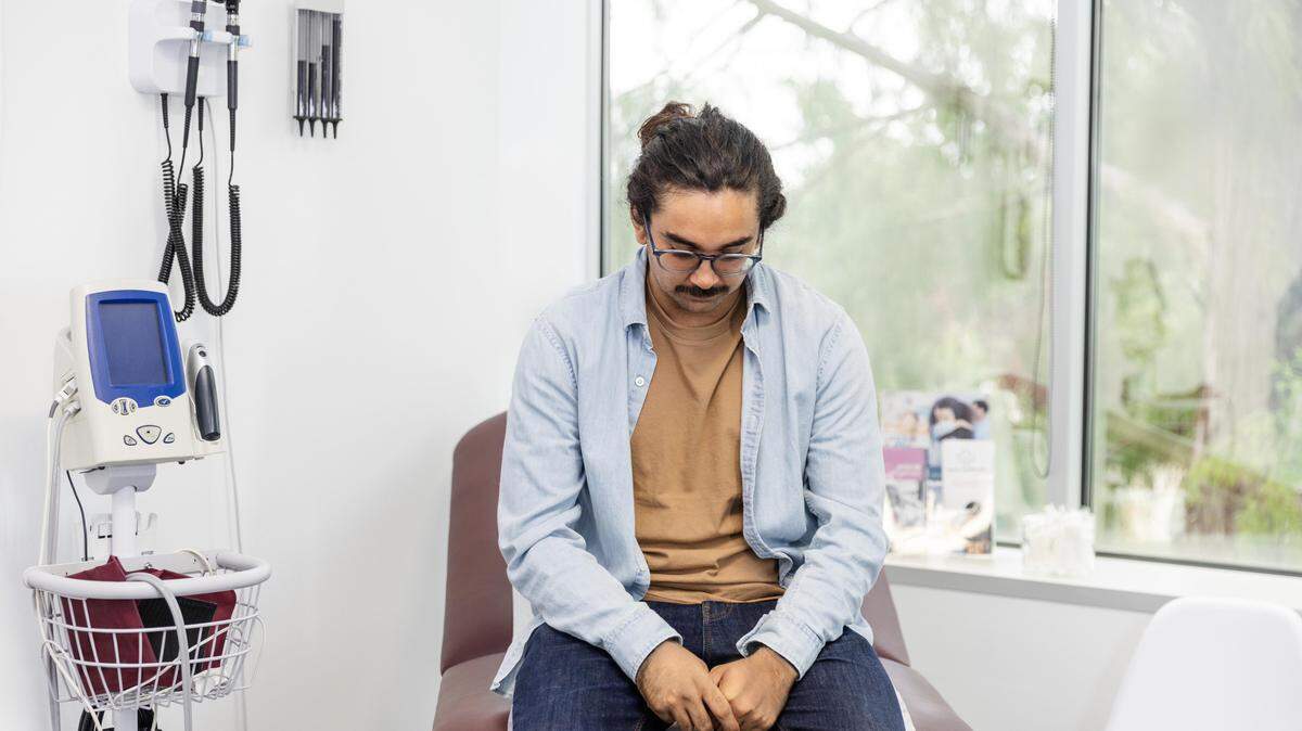 A young man sitting in a doctor's exam room looking anxious.