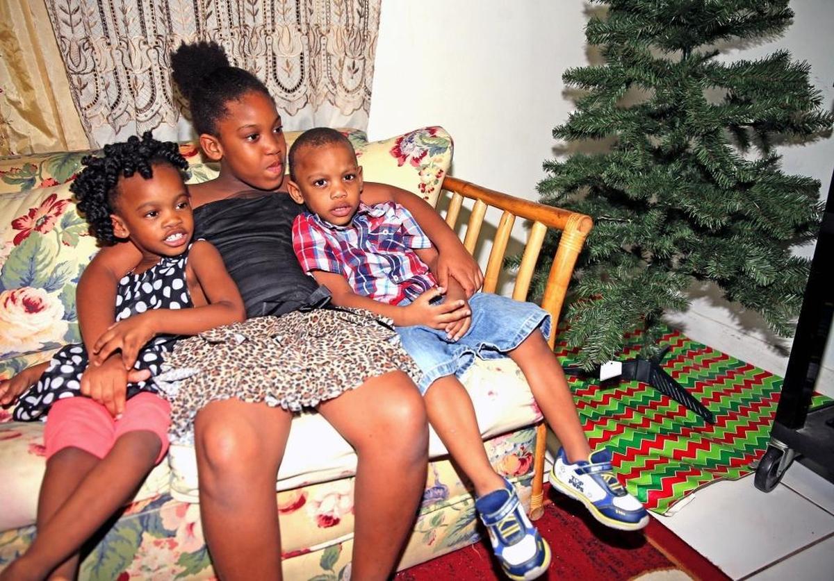 Adrienne Grant-Simpson’s children, Danila 3, Adrianna 7, and Daniel 3, sit on the couch next to the Christmas tree with no gifts in their Sunrise home on Nov. 30.