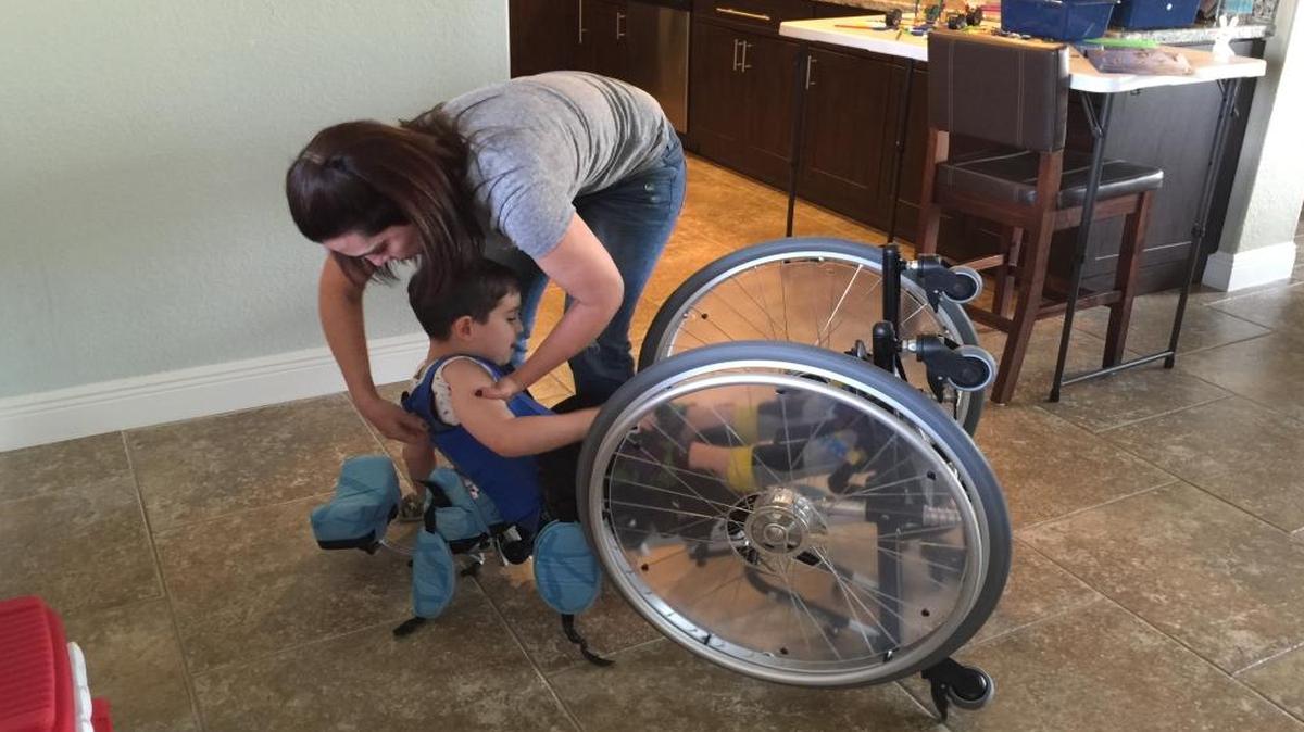 Diana Miranda-Martinez, Manny’s mom, helps him get out of his wheelchair so he can crawl around and play with his brother in their Hialeah home.