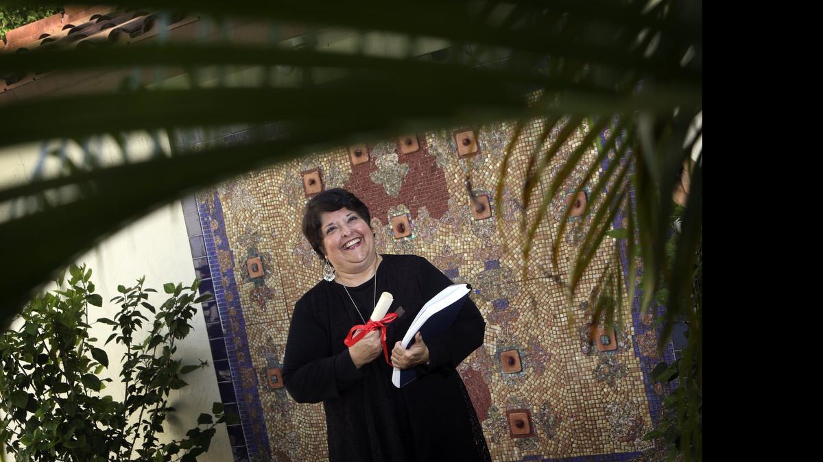 
Genie Milgrom stands in the backyard of her Pinecrest home in front of a mosaic that she created that is the “Moroccan Carpet.” Milgrom, a Cuban woman who was raised Catholic, converted to Judaism after she began researching her maternal lineage to find that her family was persecuted by the Inquisition in a little town on the border of Spain and Portugal. She holds a symbolic key given to her of the Jewish quarter of the village in Fermoselle, Spain, where her family was. She also holds a large book that is just some of the supporting documentation for the family tree she researched.
