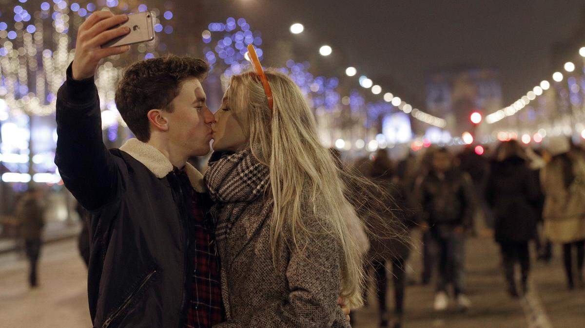 A man takes a picture as he kisses his companion during the New Year's Eve celebration on the Champs Elysees, in Paris, France, Sunday, Jan.1, 2017. (AP Photo/Christophe Ena)