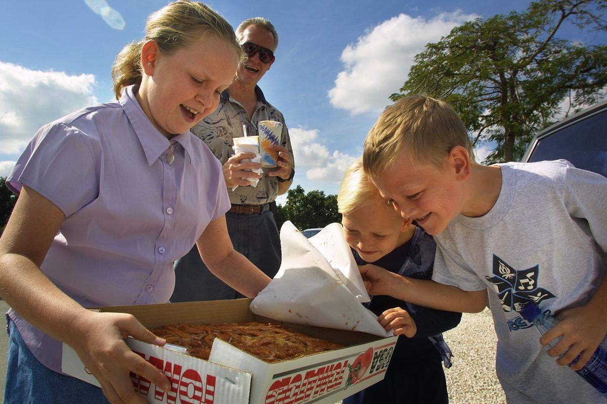 Meghan Gross, 9, left, Jennifer Gross, 6, and Ben Gross, 7, right, get a nose full of hot cinnamon rolls from Knaus Berry Farm, 15980 SW 248th Street in the Redlands, as dad, Tom Gross, holds their shakes in back. The seasonal farm draws returning crowds of people hungry for cinnamon rolls, baked goods, fresh vegetables, and strawberry shakes.