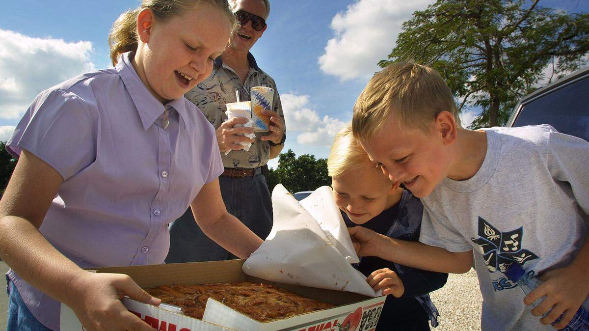 Meghan Gross, 9, left, Jennifer Gross, 6, and Ben Gross, 7, right, get a nose full of hot cinnamon rolls from Knaus Berry Farm, 15980 SW 248th Street in the Redlands, as dad, Tom Gross, holds their shakes in back. The seasonal farm draws returning crowds of people hungry for cinnamon rolls, baked goods, fresh vegetables, and strawberry shakes.