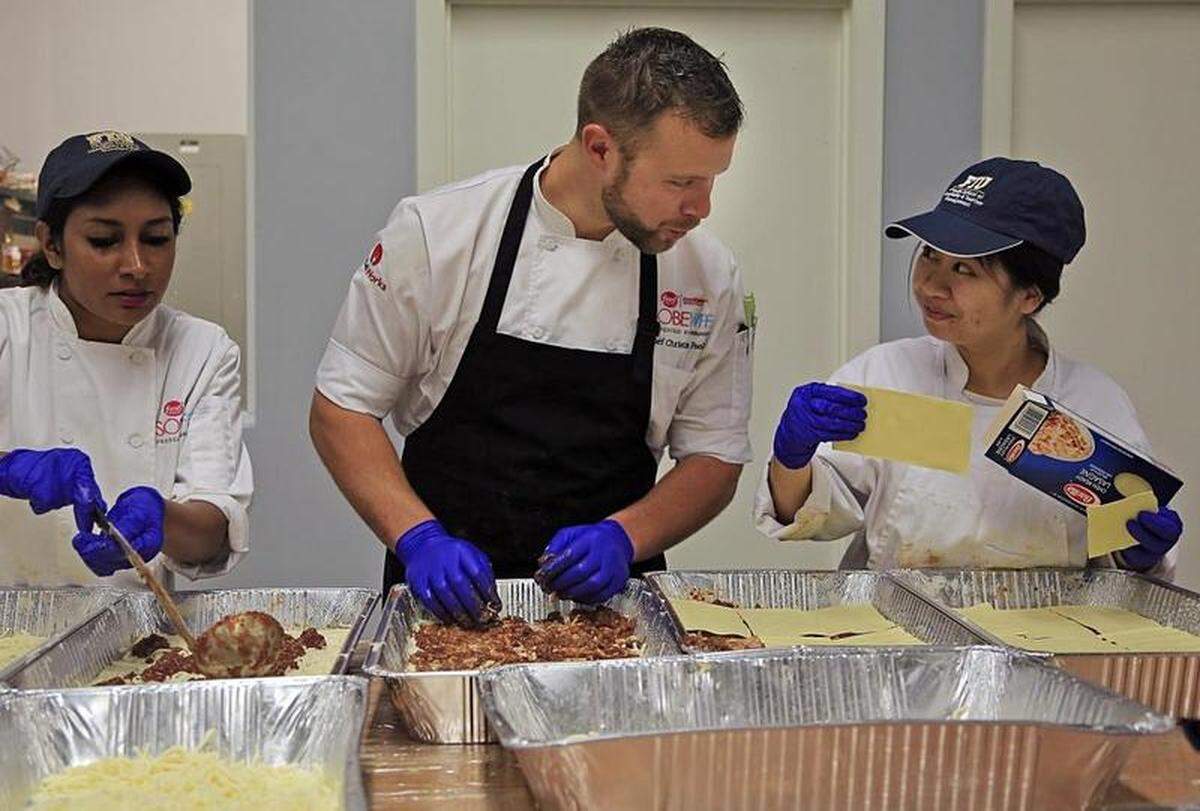 Just on the other side of the alley where as many as 700 people a night are cooked a free meal at the Miami Rescue Mission, chefs in town for the South Beach Wine &amp; Food Festival prep in the mission’s multipurpose space for various festival events this week. FIU culinary students, Rebecca Masihdas, junior, left, and Shenglei Wong, right, assist chef Christian Poole, center, in preparing lasagna for the festival’s Italian Bites on the Beach event.