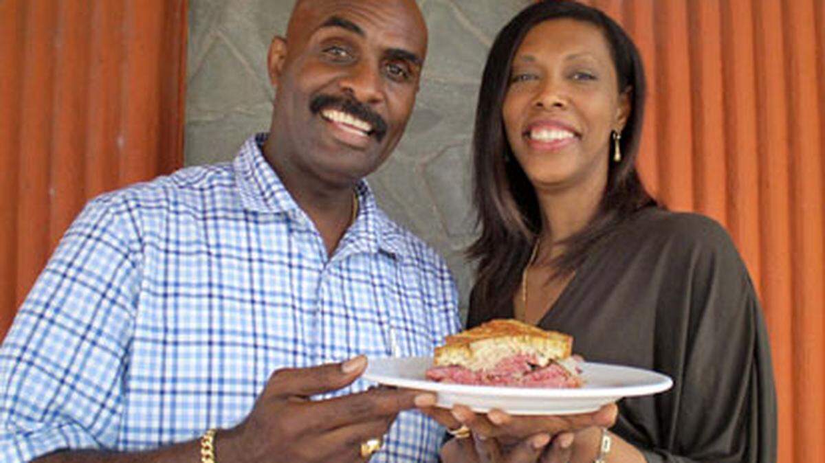 J.J. and wife Claudie Jean-Charles hold a signature Reuben sandwich in front of Stephen's New York Style Deli in Hialeah which they own and run. Linda Bladholm.