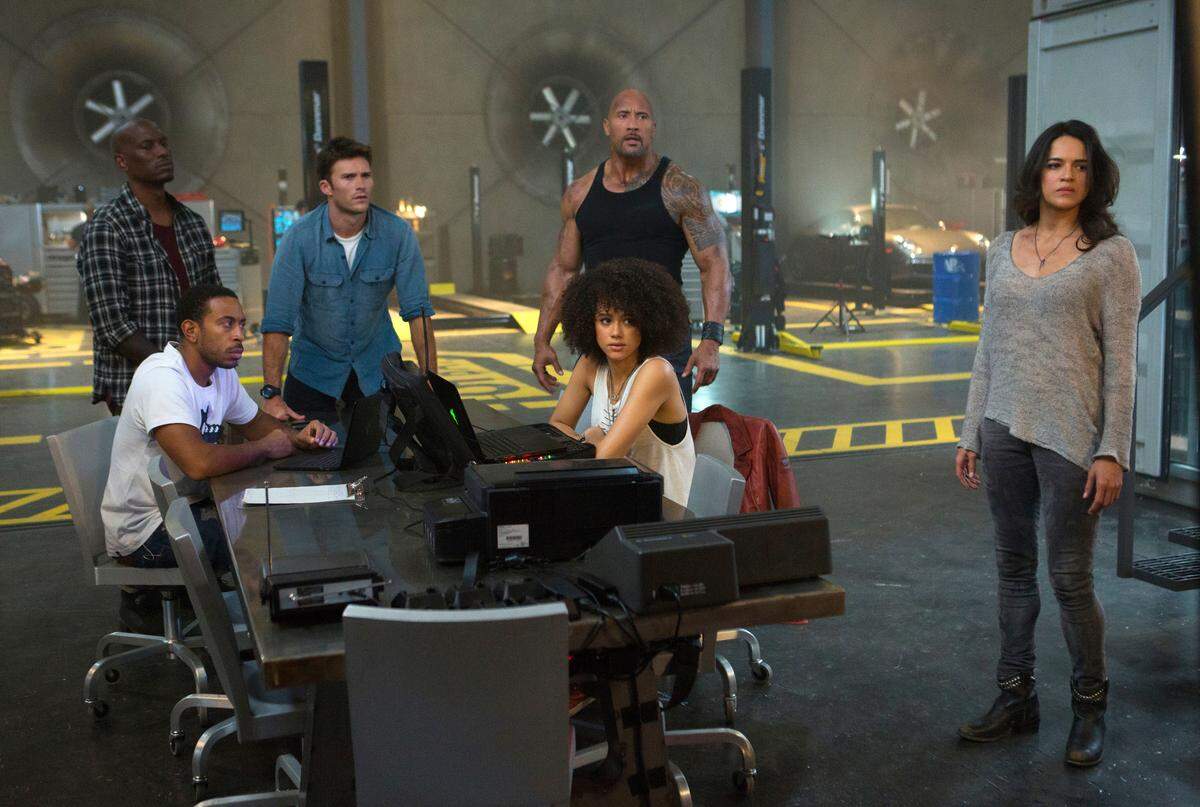 This image released by Universal Pictures shows, Chris "Ludacris" Bridges, seated left, and Nathalie Emmanuel, seated right, and Tyrese Gibson, standing from left, Scott Eastwood, Dwayne Johnson and Michelle Rodriguez in "The Fate of the Furious." (Matt Kennedy/Universal Pictures via AP)