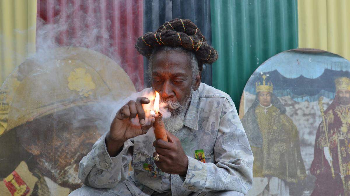 In this Aug. 28, 2014 photo, legalization advocate and reggae legend Bunny Wailer smokes a pipe stuffed with marijuana during a “reasoning” session in a yard in Kingston, Jamaica, decorated with Rastafarian colors and images of former Ethiopian Emperor Haile Selassie. Wailer, a founder of the iconic Wailers reggae group with late superstars Bob Marley and Peter Tosh, and fellow Rastafarians have long called for legalization of the drug that they smoke as part of their spiritual worship. Now, many Rastas are welcoming plans by the Jamaican government to decriminalize marijuana for religious purposes, among other proposed amendments to the island’s drug laws. (AP Photo/David McFadden)