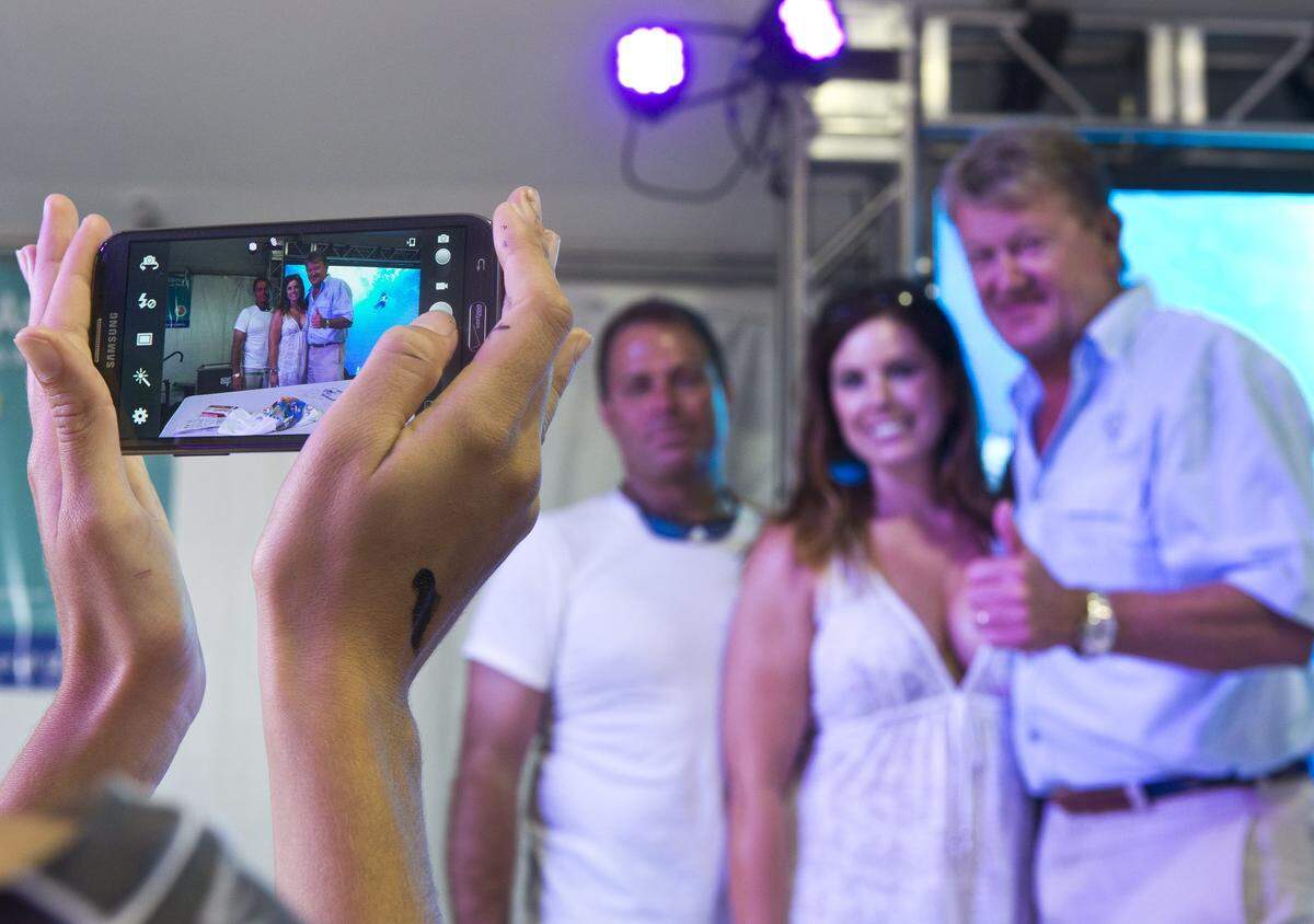 Mike Lank and Angela Williams, from Virginia, have their photo taken with Guy Harvey in the Conservation Village at the Rock The Ocean’s Tortuga Music Festival on Ft. Lauderdale beach on Saturday, April 13, 2013.