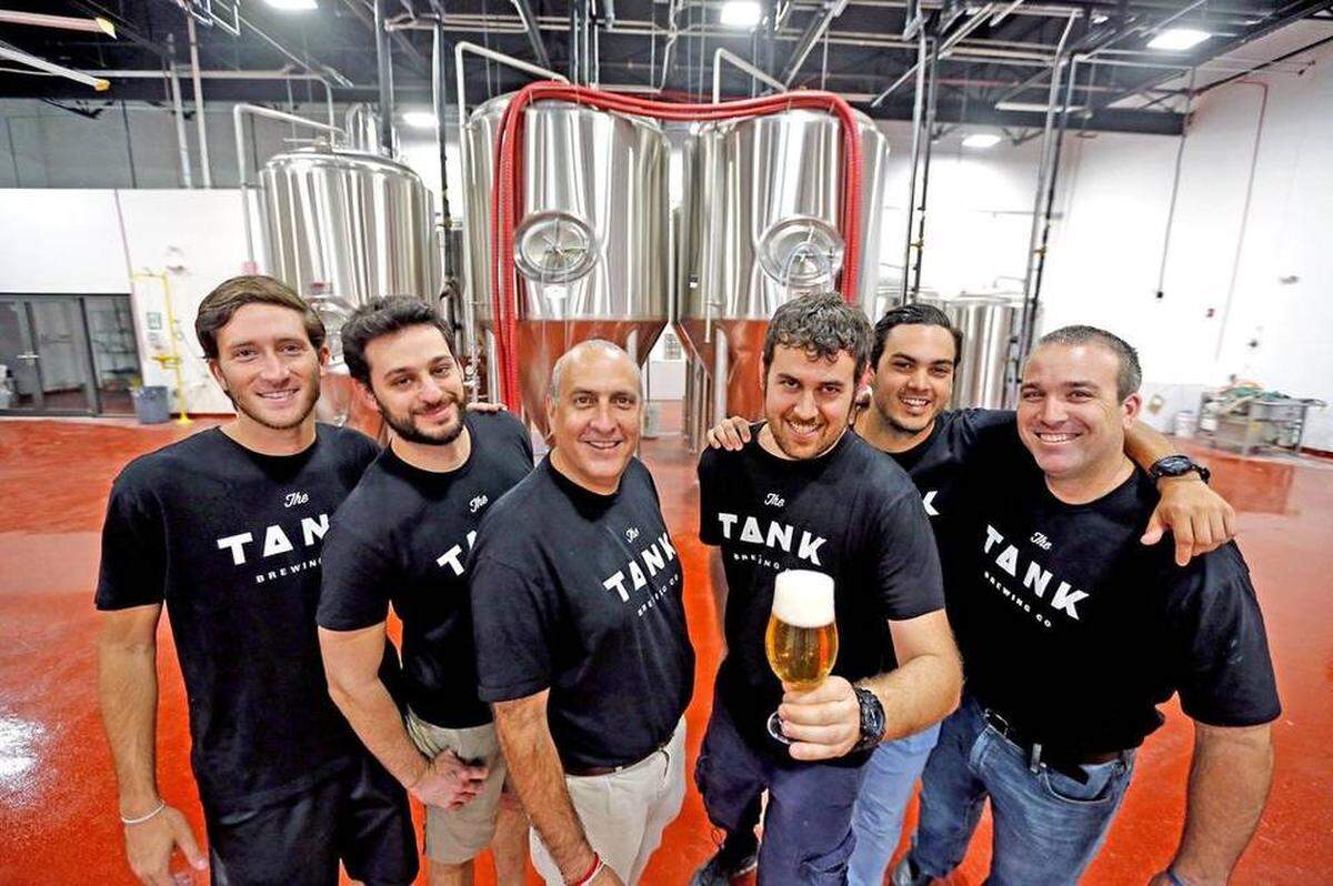 Owner Carlos Padron, left-center, between Matthew Weintraub, right-center, and Moh , with their crew at the The Tank Brewing Company. The company was founded by cigar aficionado Padron and young head brewer Weintraub, formerly of FIU’s brewing program.