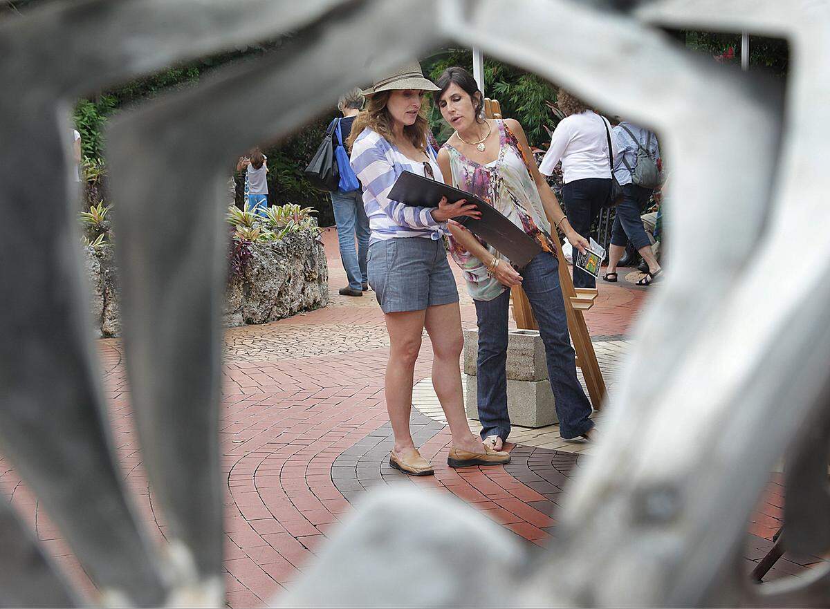 Peering through Alfredo Alea's sculpture, "Sowing", Miami resident Lourdes Reyes, left, looks over her sister's work (right- she refused to give her name), as Reyes visits her booth at the art fair.  On Sunday, January 10, 2014 12th Annual South Motors Pinecrest Gardens Fine Arts Festival where 65 artists will exhibited their works among 14 acres of native forested wetland, tropical hardwood hammock and native cypress slough hammock.