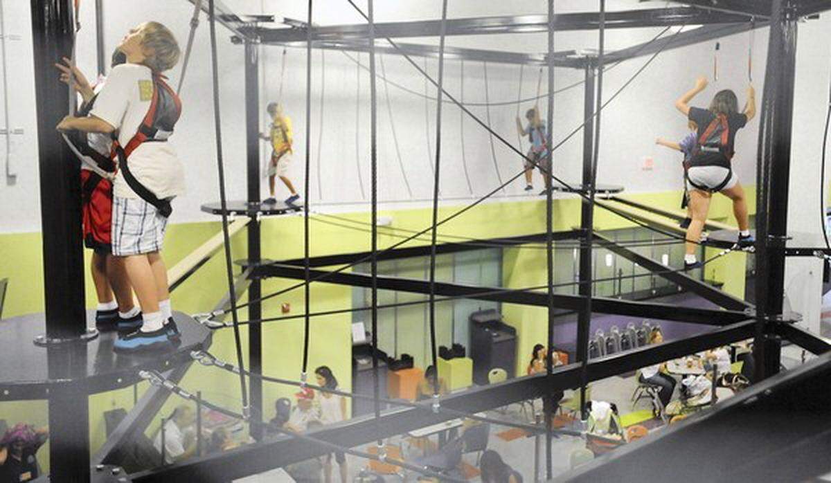 Children clim in harnesses along cables above as parents grab a bite to eat in the cafeteria below at Funderdome in Fort Lauderdale. This is part of a series of indoor activities folks can do in the summer; new places that have opened. One of them is the Funderdome, an indoor play area that has rock climbing, a lazer challenge, and all kinds of colorful, electronic gadgets. 8/6/11. Jim Rassol, Sun Sentinel.