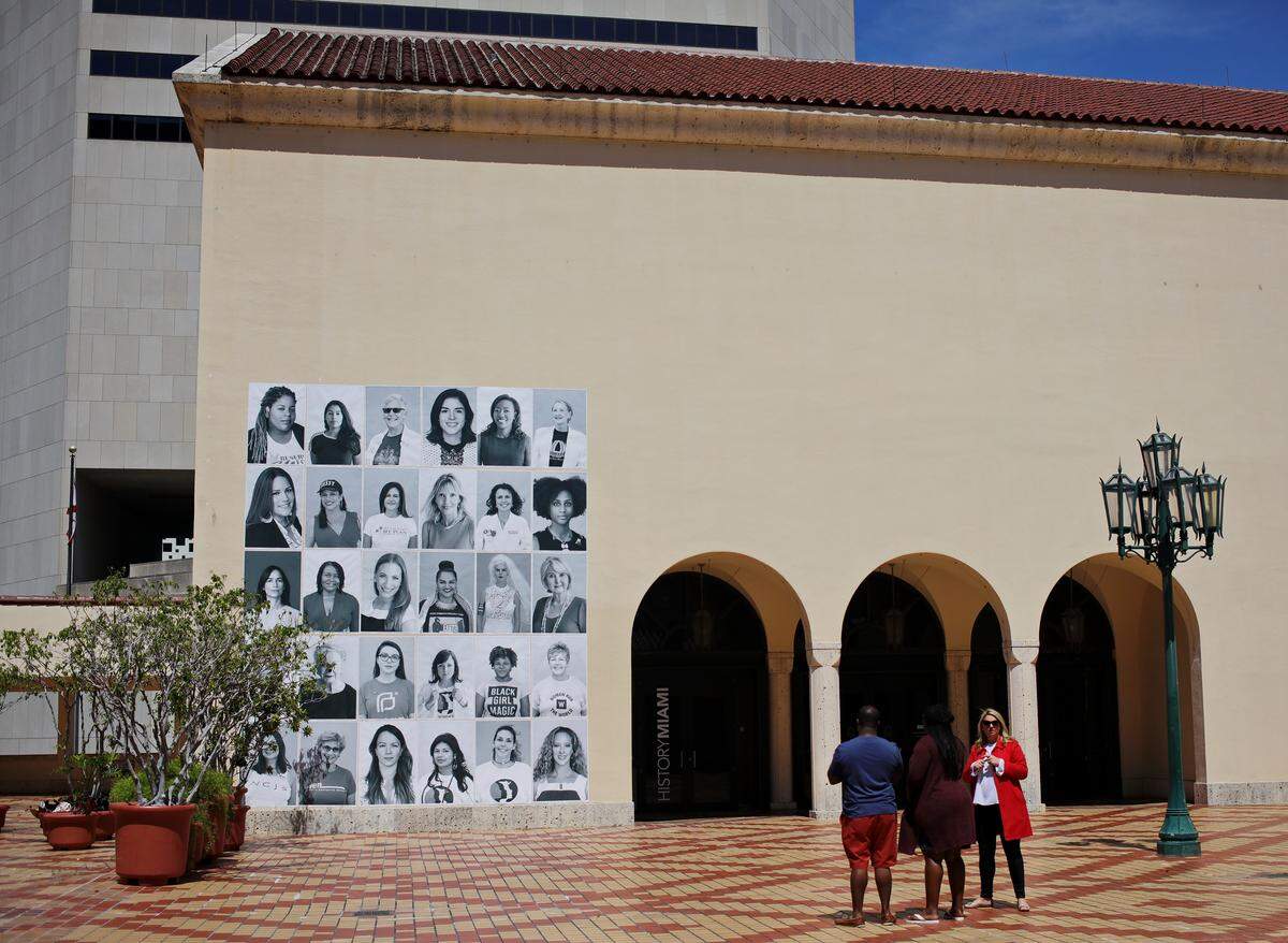 A group gathers to look at "Miami Girls Make History" outside of HistoryMiami.