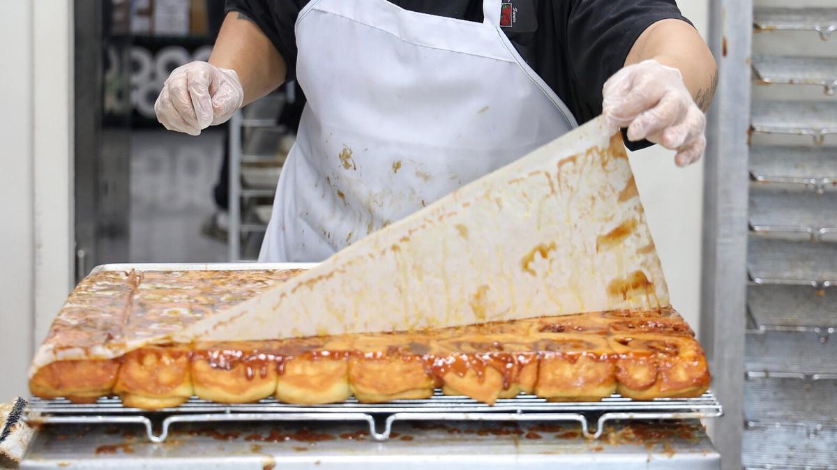 Baker assistant Danny Gonzalez, 20, flips a batch of hot cinnamon rolls as a long line forms outside Knaus Berry Farm in the Redland, which opened Tuesday, Oct. 29, 2019. The opening of Knaus signals the start of the fall in South Florida.