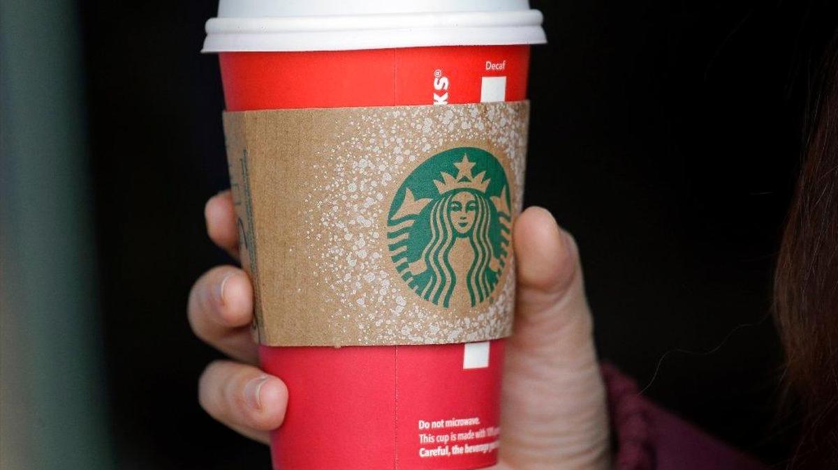 A customer carries a coffee drink in a red paper cup, with a cardboard cover attached, outside a Starbucks coffee shop in the Pike Place Market, Tuesday, Nov. 10, 2015, in Seattle. Starbucks’ minimalist new holiday coffee cup has set off complaints that the chain is making war on Christmas.