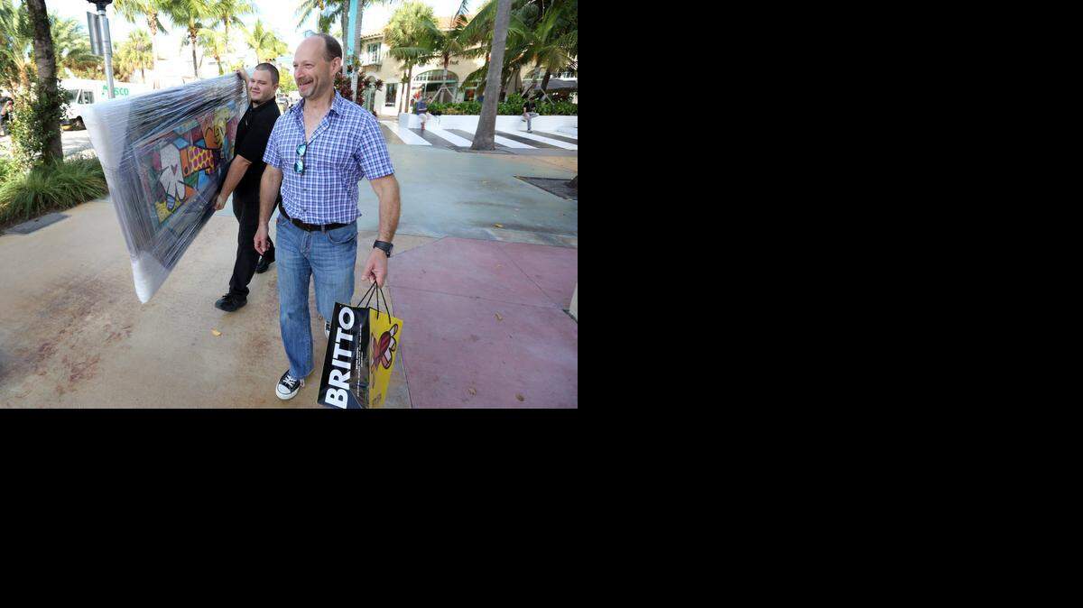 
Nate Paulding, a Britto Central inventory supervisor, carries a large painting, titled 'The Hug,' along Lincoln Road for customer Steve Yucht. Yucht, of Gainesville, bought the large painting as a surprise for his wife for the holidays. Shoppers were out along Lincoln Road Tuesday morning, Dec. 23, 2014, getting their last-minute Christmas gifts.

