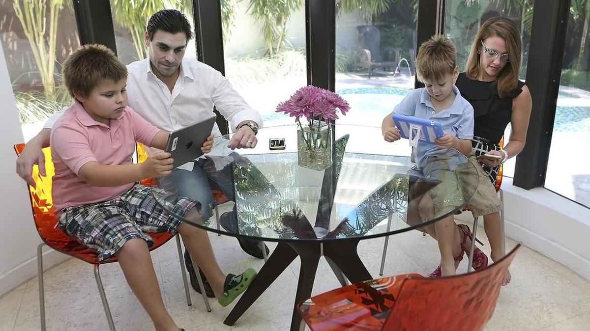 Brian and Elisa D’Amico, with sons Sam, 8, left, and Joseph, 4, gather around the kitchen table with electronic devices.