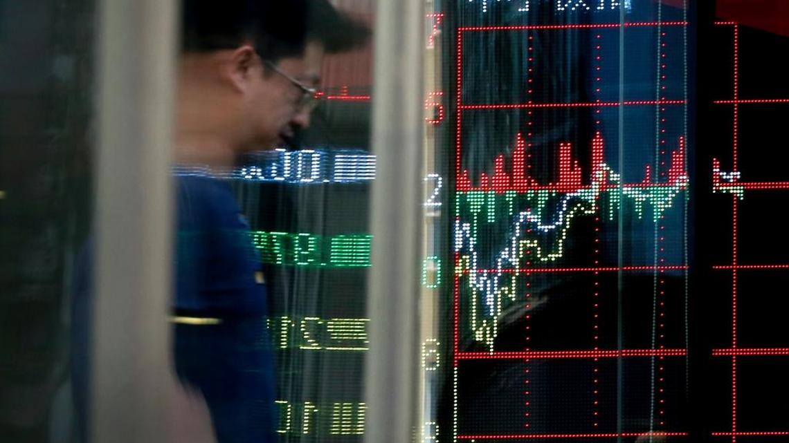 A man is reflected on a glass panel as he walks past an electronic board displaying stock trading index at a brokerage house in Beijing on May 24.