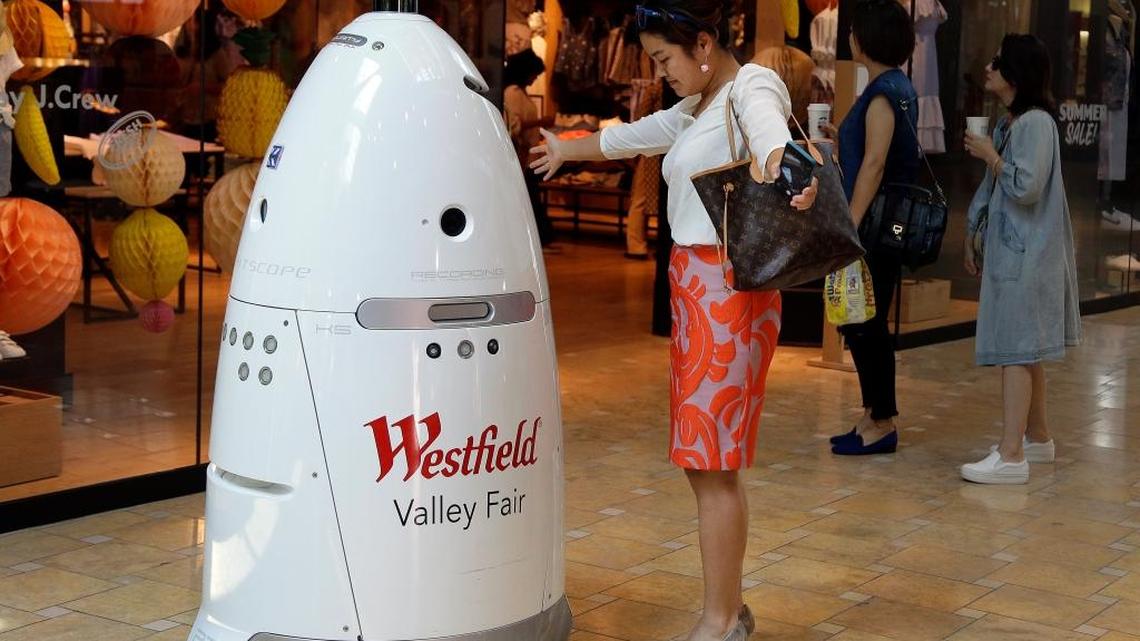 In this Monday, June 26, 2017, photo, Sophie Li, of Cupertino, Calif., offers to dance with a K5 robot made by Knightscope, Inc., at Westfield Valley Fair shopping center in San Jose, Calif. In the technology hotbed that stretches from San Francisco to San Jose, people can eat a pizza made largely by a robot, have hotel toiletries delivered by a robot, drink a frothy cappuccino made by a robot and shop at a mall with robot security.