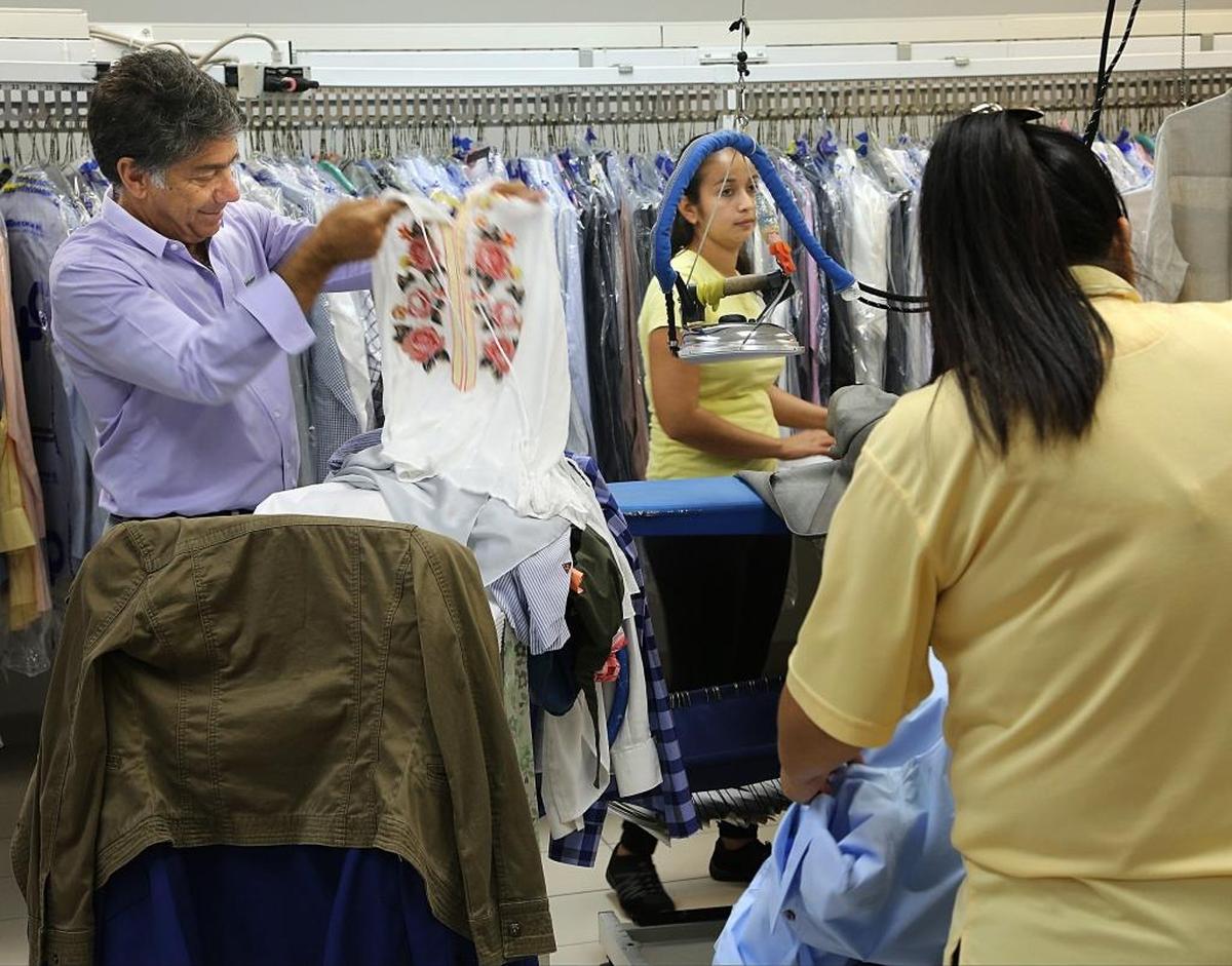 Salomon Mishaan, president of OXXO Care Cleaners in Hollywood, inspects a newly cleaned item as Brenda Amaya, center, and Mariela Gonzalez iron garments.