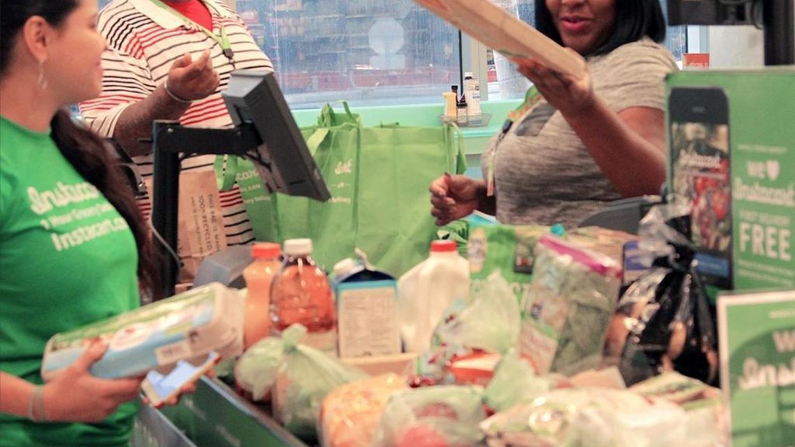 Claudia Rodas, Instacart “shift lead,” left, doublechecks a customer’s order as Personal Shopper Joel King, center, and Louna Nelson, right, complete the customer’s order. On Dec. 7, Instacart shoppers bagged orders at the register for delivery in the Whole Foods Market in downtown Miami.