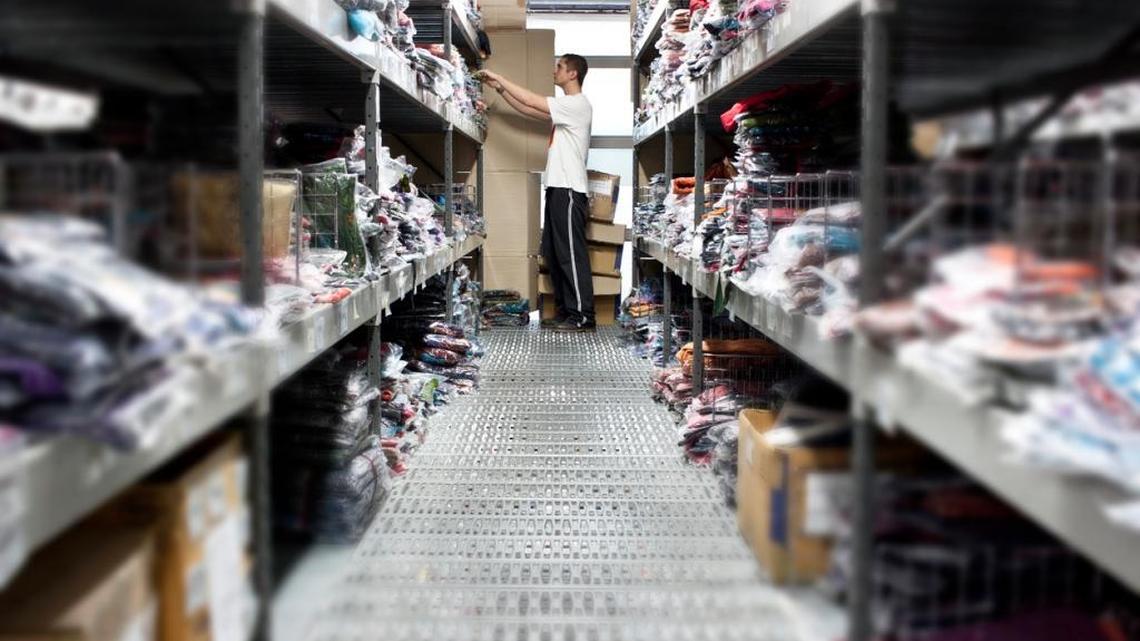 Stock boy browsing throught a shelf in a clothes-wholesaling warehouse.