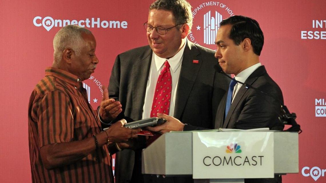 HUD Secretary Julian Castro (right) and Comcast senior executive David Cohen give a free laptop and six months of free Internet service to Rochenel Jean Baptiste at a press conference at Rainbow Village Public Housing Development. The press conference introduced a Comcast pilot program that will expand its highly successful low-cost Internet Essentials program to all public housing residents of Miami-Dade.